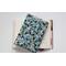 A padded book sleeve on top of an open book. The book sleeve is made with a blue floral Rifle Paper Co. cotton print.