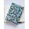 A padded book sleeve on top of an open book. The book sleeve is made with a blue floral Rifle Paper Co. cotton print.