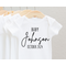 white baby bodysuit with Baby at top, then last name of family and month and year of baby's birth. in black print. in long or short sleeves