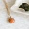Sunstone necklace, orange briolette in 14K gold, on white dish with green leaves.