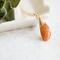 Sunstone necklace, orange briolette in 14K gold, on white dish with green leaves.