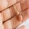 Sunstone necklace, orange briolette in 14K gold, held in hand on white background.
