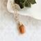 Sunstone necklace, orange briolette in 14K gold, on white dish with green leaves.