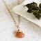 Sunstone necklace, orange briolette in 14K gold, on white dish with green leaves.