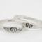 Two sterling silver rings with hand-stamped baby feet and wings, placed on a white wooden surface with delicate white flowers.
