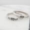 Two sterling silver rings with hand-stamped baby feet and wings, placed on a white wooden surface with delicate white flowers.
