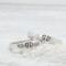 Two sterling silver rings with hand-stamped baby feet and wings, placed on a white wooden surface with delicate white flowers.
