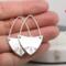 Handcrafted sterling silver fern-stamped hoop earrings held in a hand showcasing elegant leaf designs. 
