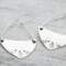 Handcrafted sterling silver fern-stamped hoop earrings on a wooden surface, showcasing elegant leaf designs. 
