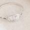 Handcrafted sterling silver wildflower oval cuff bracelet from Alaska, with textured band, on floral paper. 
