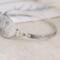 Handcrafted sterling silver wildflower oval cuff bracelet from Alaska, with textured band, on floral paper. 
