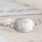 Handcrafted sterling silver wildflower oval cuff bracelet from Alaska, with textured band, on floral paper. 
