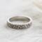 Detailed view of a sterling silver floral ring on wood, emphasizing its unique 4mm texture.
