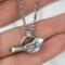  Hand holding a sterling silver bird necklace with turquoise, against green leaves.
