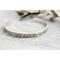 A single sterling silver cuff bracelet with intricate floral engravings, styled with soft natural elements in the background.