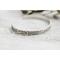 A single sterling silver cuff bracelet with intricate floral engravings, styled with soft natural elements in the background.