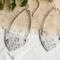 Handcrafted sterling silver Art Nouveau floral hoop earrings on a textured background with greenery.
