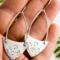 Handcrafted sterling silver Art Nouveau floral hoop earrings held in a hand with a background with greenery.
