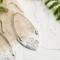 Handcrafted sterling silver Art Nouveau floral hoop earrings on a textured background with greenery.
