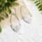 Handcrafted sterling silver Art Nouveau floral hoop earrings on a textured background with greenery.
