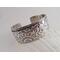 Wide sterling silver bracelet with floral textured overlay.