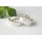"Two silver bands with personalized engraving, 'JOHN' and 'PSALMS" visible, on a white fabric with green leaves in the background."
