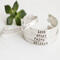 Five sterling silver bracelets with words HOPE, LOVE, GRACE, FAITH, BELIEVE, on a white surface with a green succulent in the background.
