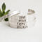 Five sterling silver bracelets with words HOPE, LOVE, GRACE, FAITH, BELIEVE, on a white surface with a green succulent in the background.
