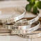 Five sterling silver bracelets with words HOPE, LOVE, GRACE, FAITH, BELIEVE, on a wood surface with a green succulent in the background.
