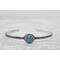 Silver bracelet with floral engravings, featuring a oval blue aquamarine on a light wood surface with scattered white baby's breath flower.
