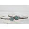 Silver bracelet with floral engravings, featuring a oval blue aquamarine on a light wood surface with scattered white baby's breath flower.
