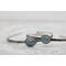 Silver bracelet with floral engravings, featuring a oval blue aquamarine on a light wood surface with scattered white baby's breath flower.
