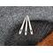 Three bone nalbinding needles on a background of black, gray, and brown nalbound fabric.