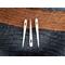 Three bone nalbinding needles, laying on a background of black and brown nalbound fabric.