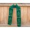 Green scarf with trees along the length. It is on a hanger in front of a wooden fence.