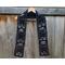 Black scarf with ghosts along the length. It is on a hanger in front of a wooden fence.