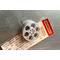 front view of a silver miniature movie reel magnet holding up a movie ticket on fridge