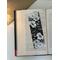 black and white floral bookmark on a book on a white table. Light brown table runner with fairy lights in a jar
