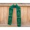 Green scarf with trees along the length. It is on a hanger in front of a wooden fence.