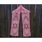 Pink scarf with hearts along the length. It is on a hanger in front of a wooden fence.