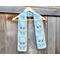 Display of the Flower Crochet Scarf on a hanger in front of a wooden fence.