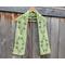 Display of the Leaf Crochet Scarf on a hanger in front of a wooden fence.