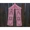 Pink scarf with hearts along the length. It is on a hanger in front of a wooden fence.