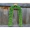 Variegated green scarf with trees along the length. It is on a hanger in front of a wooden fence.