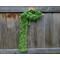 Variegated green scarf with trees along the length. It is on a hanger in front of a wooden fence.