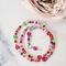 Pink and green glass beaded choker necklace, next to a flower.