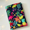 This tropical book sleeve has navy background with flamingos, tropical leaves and flowers in bright colors