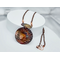 Round copper pendant colored in deep shades of red, blue, yellow created by flame coloring hanging under oval copper piece on copper chain
