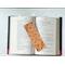 the laminated bookmark is in the middle of an open book with fairy lights around the book on a white table