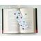 the hot cocoa bookmark is in the middle of an open book with fairy lights above on a white table